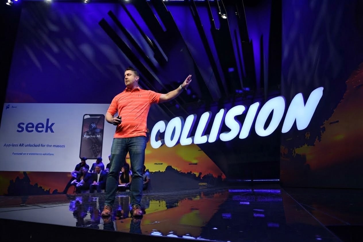 Jon Cheney pitching Seek on the Collision main stage, beside the COLLISION sign